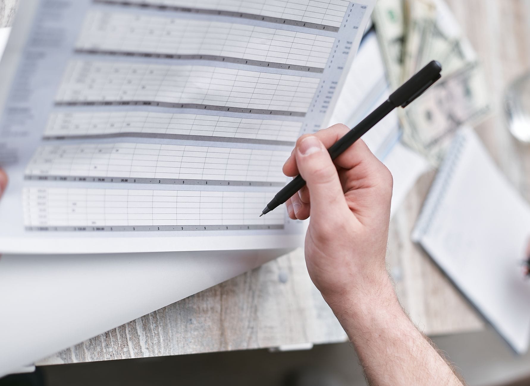 Arkusz do planowania nauki języków w Google Sheets z dziennikiem postępów Osoba z długopisem analizuje dokument finansowy z banknotami obok