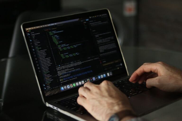 Dłonie programisty piszącego kod na laptopie