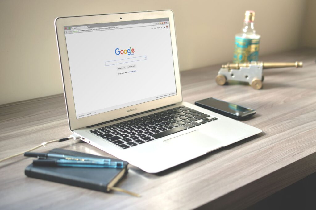 Laptop z wyszukiwarką Google, smartfon i notatnik na drewnianym biurku